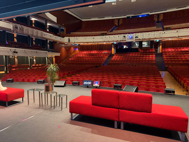 Wide view of a large theater auditorium with rows of audience seating and a professionally illuminated stage.