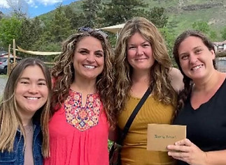Four smiling Compass Montessori parents pose together, celebrating the school’s supportive community and delivering end of year gifts.