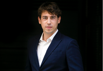 Portrait of a man in a navy blue suit and white shirt.