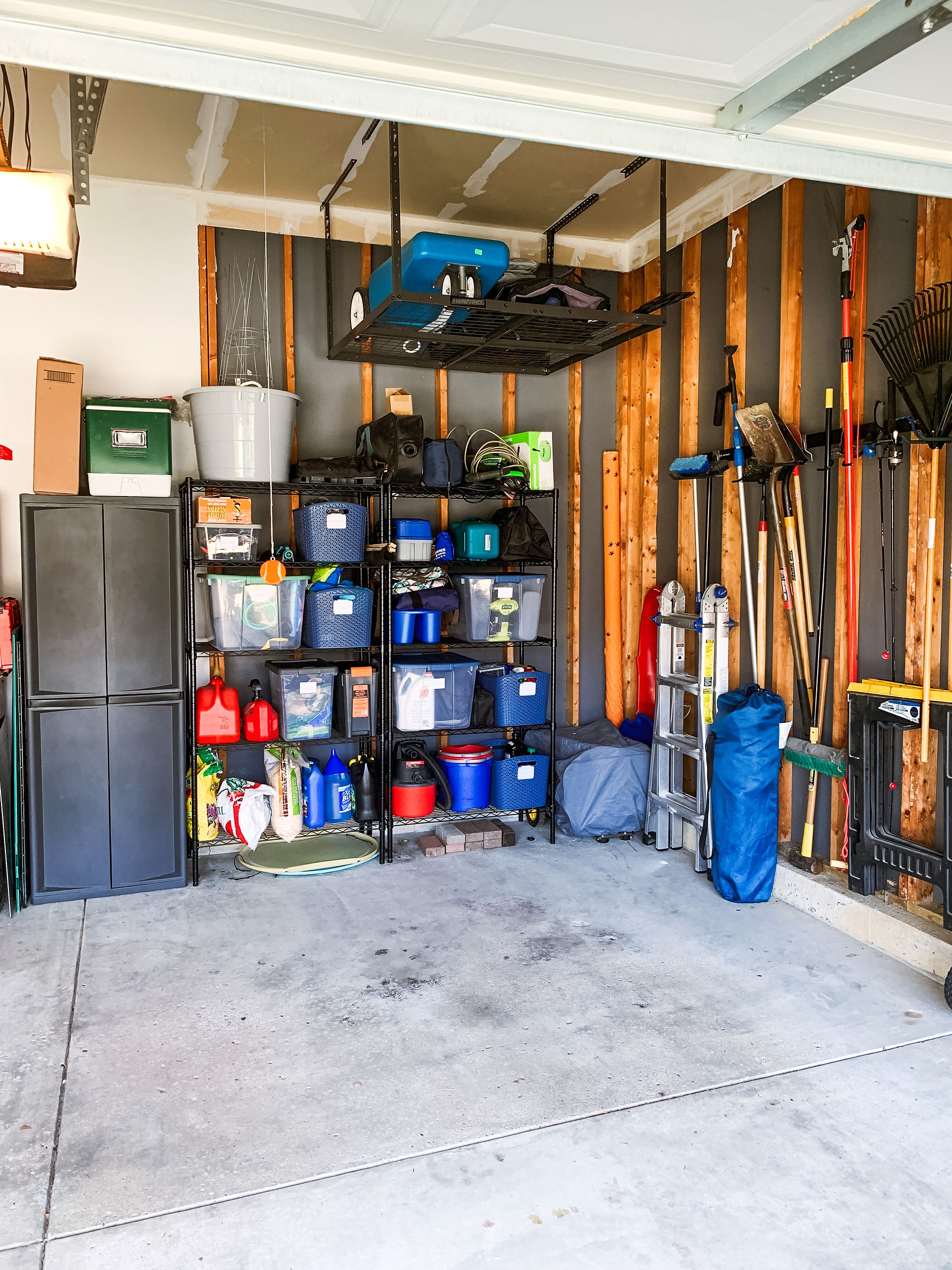 Organized garage with grey cabinet, shelving, and hanging yard tools