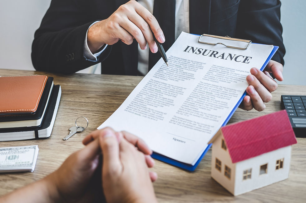 Person in suit discusses an insurance document with another. Table holds keys, model house, notebooks, cash, and calculator.