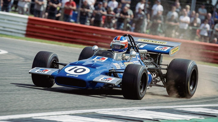 Tyrrell 701 Formula One car on track with dust flying from the rear tyres and spectators in the grandstand