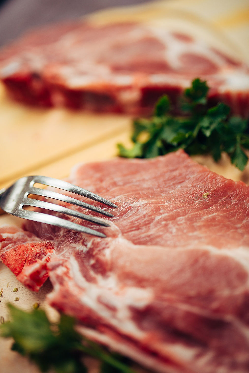 Raw bone-in pork chops with herbs on a wooden cutting board.
