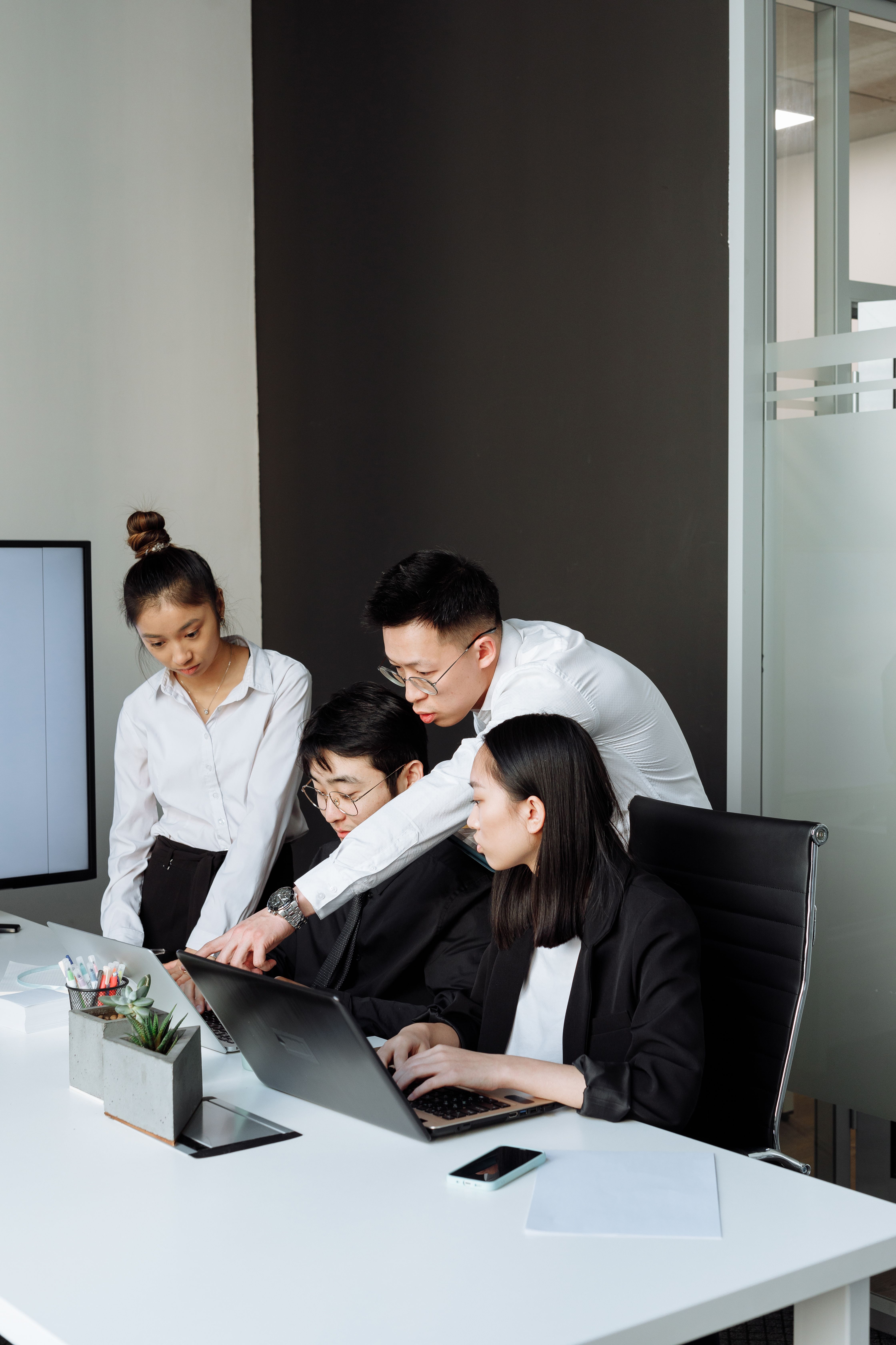 Four people gathered around laptops at an office table.
