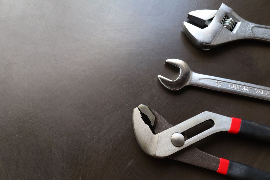 Wrenches and pliers arranged on a dark work surface.