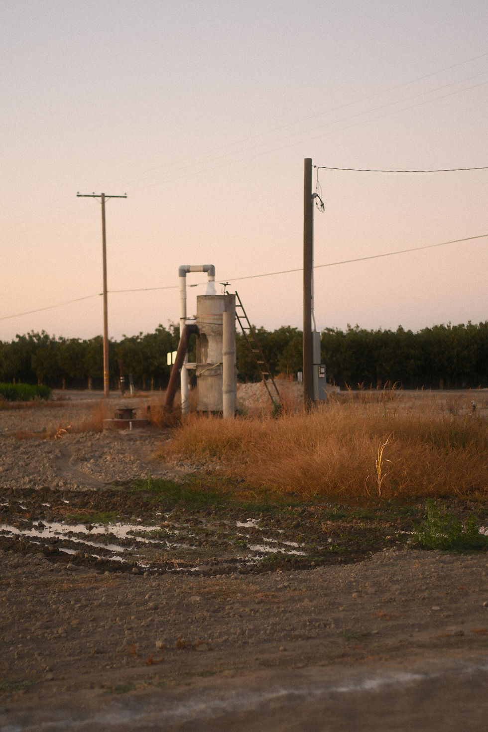 A water well pump rig standing in an open rural lot at dusk