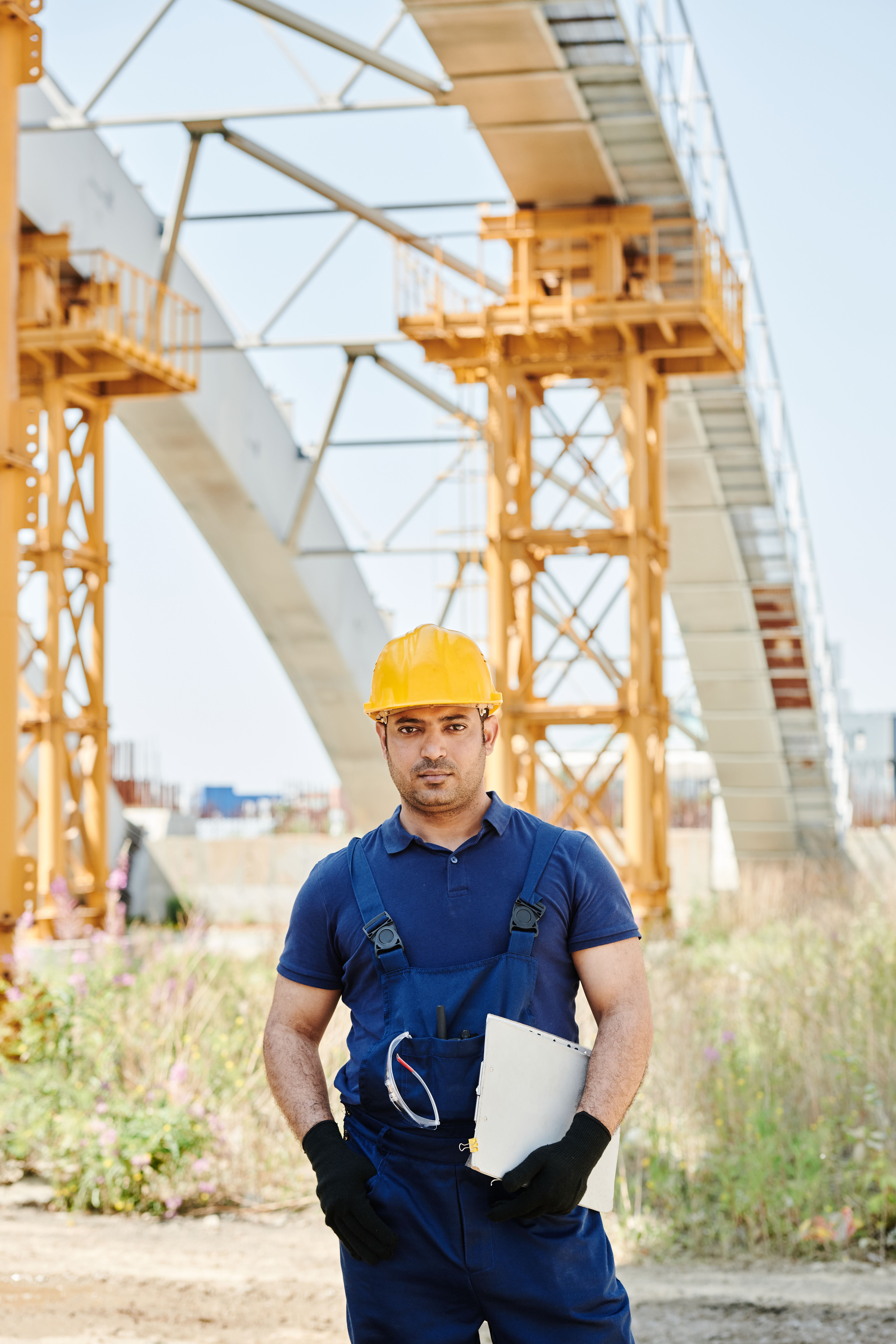 A person wearing a hard hat and holding a document folder beneath a large structure.