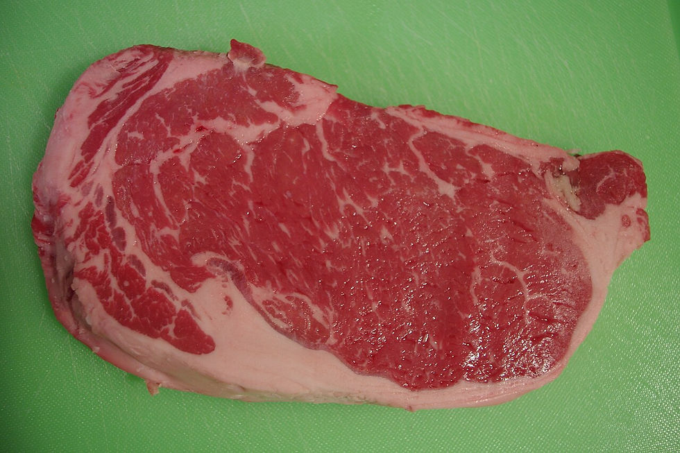 A raw marbled beef steak on a green cutting board.