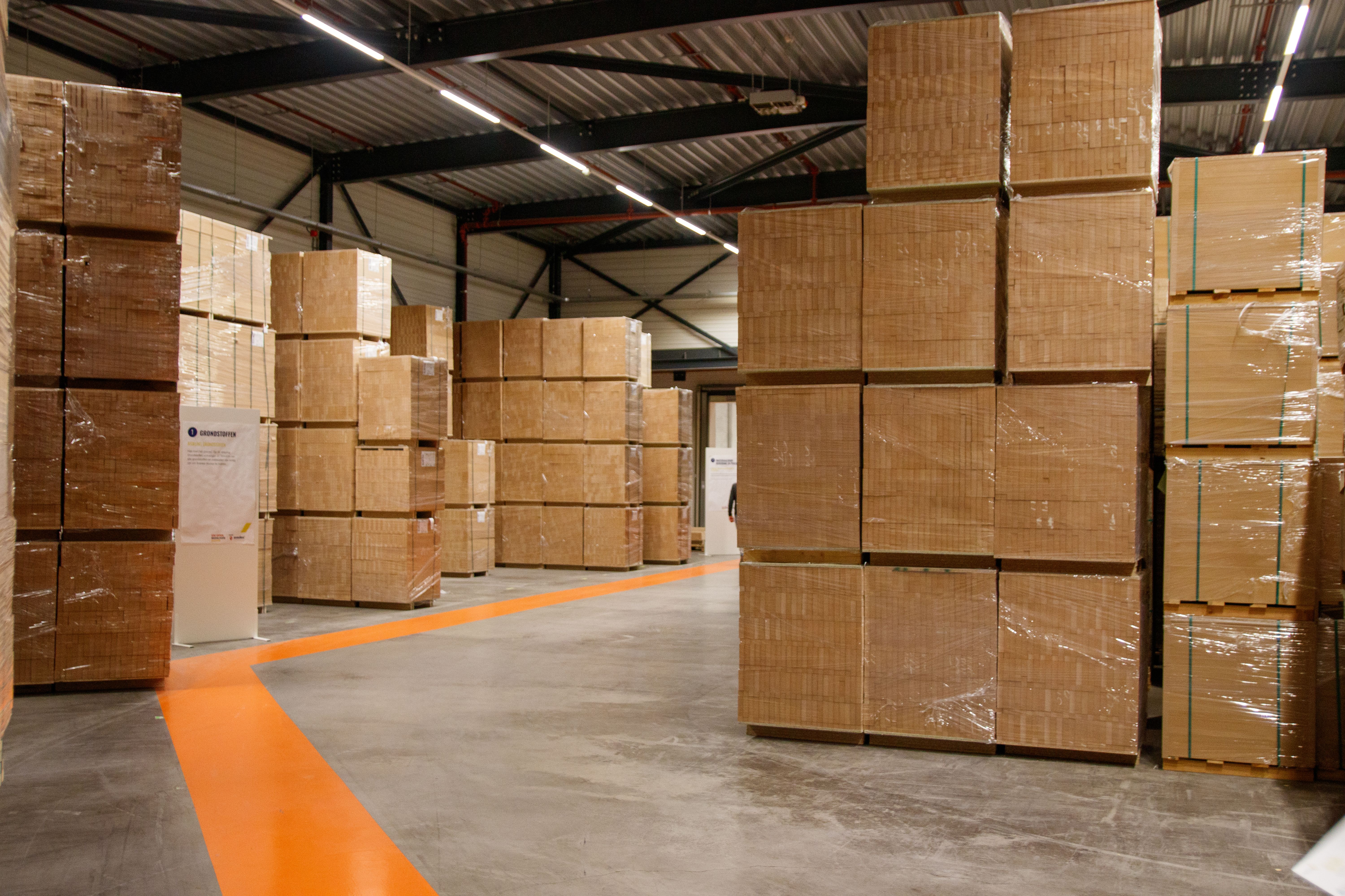 Cardboard cartons stacked beside marked aisles inside a warehouse.