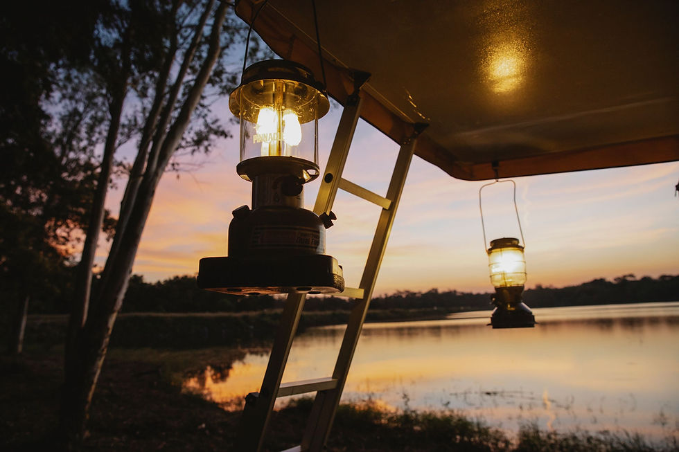 Lanterns under a camping canopy beside water at dusk; representative evening photograph.
