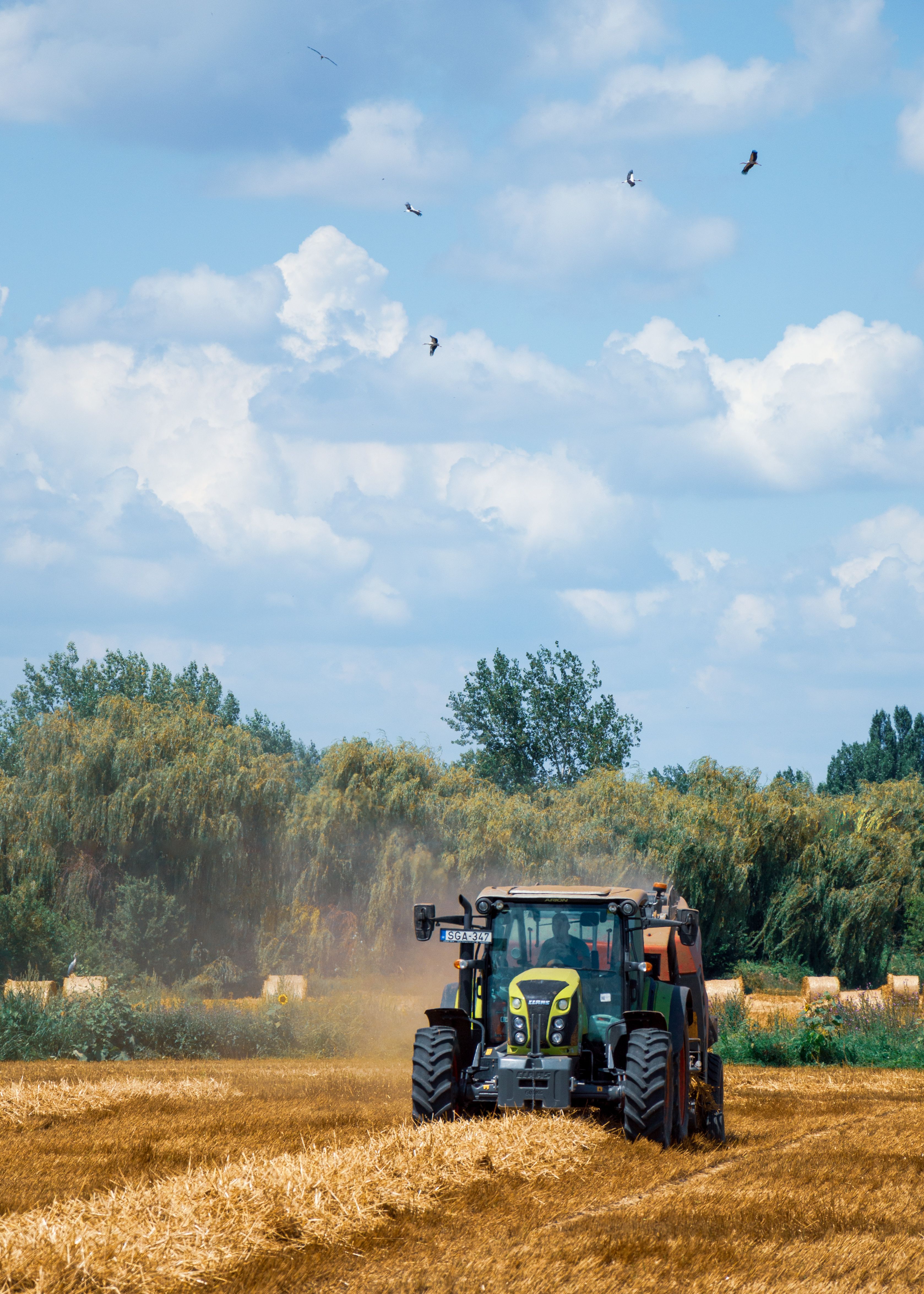 A tractor in a harvested field beneath a partly cloudy sky.