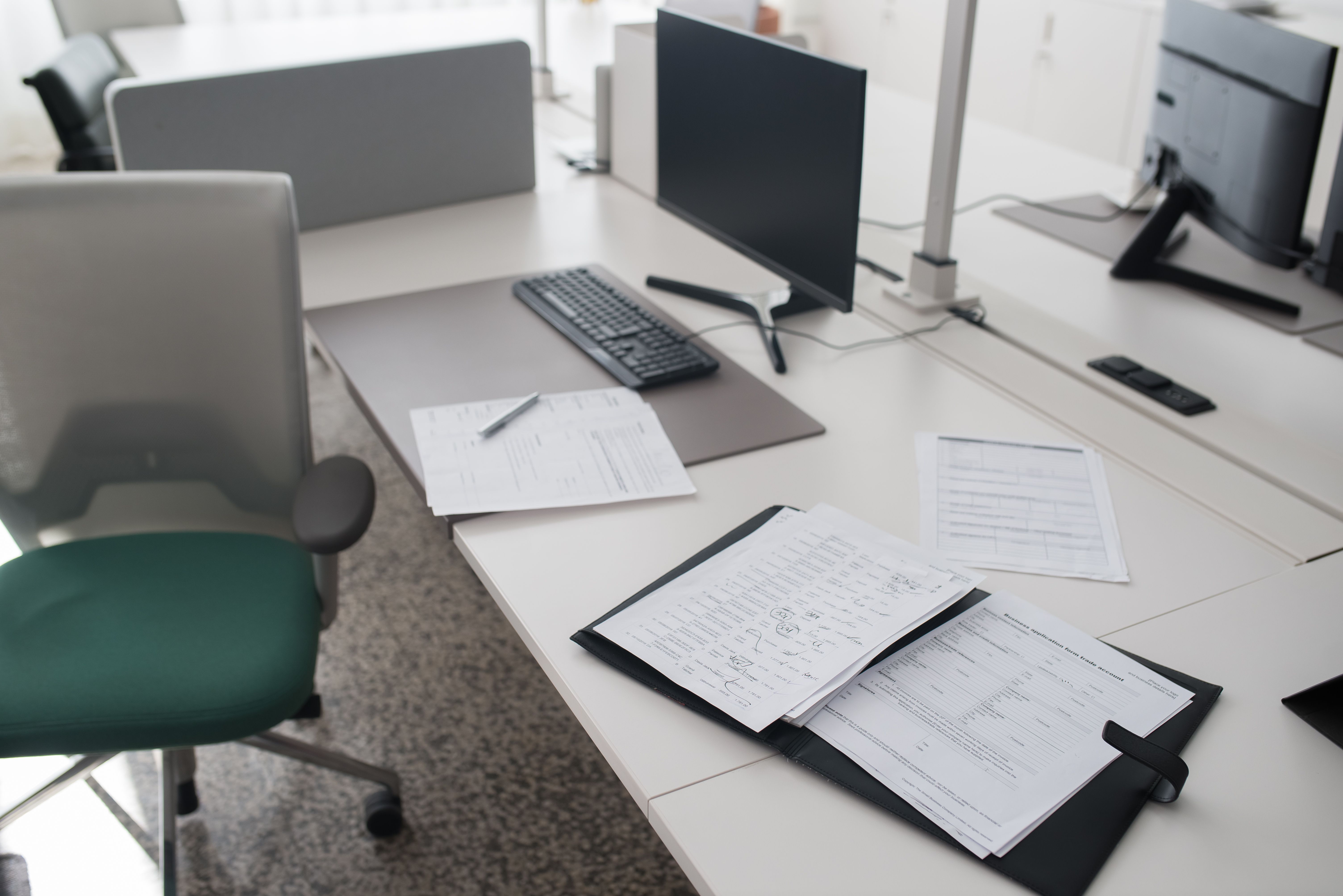An open document binder and papers on a desk beside computers.