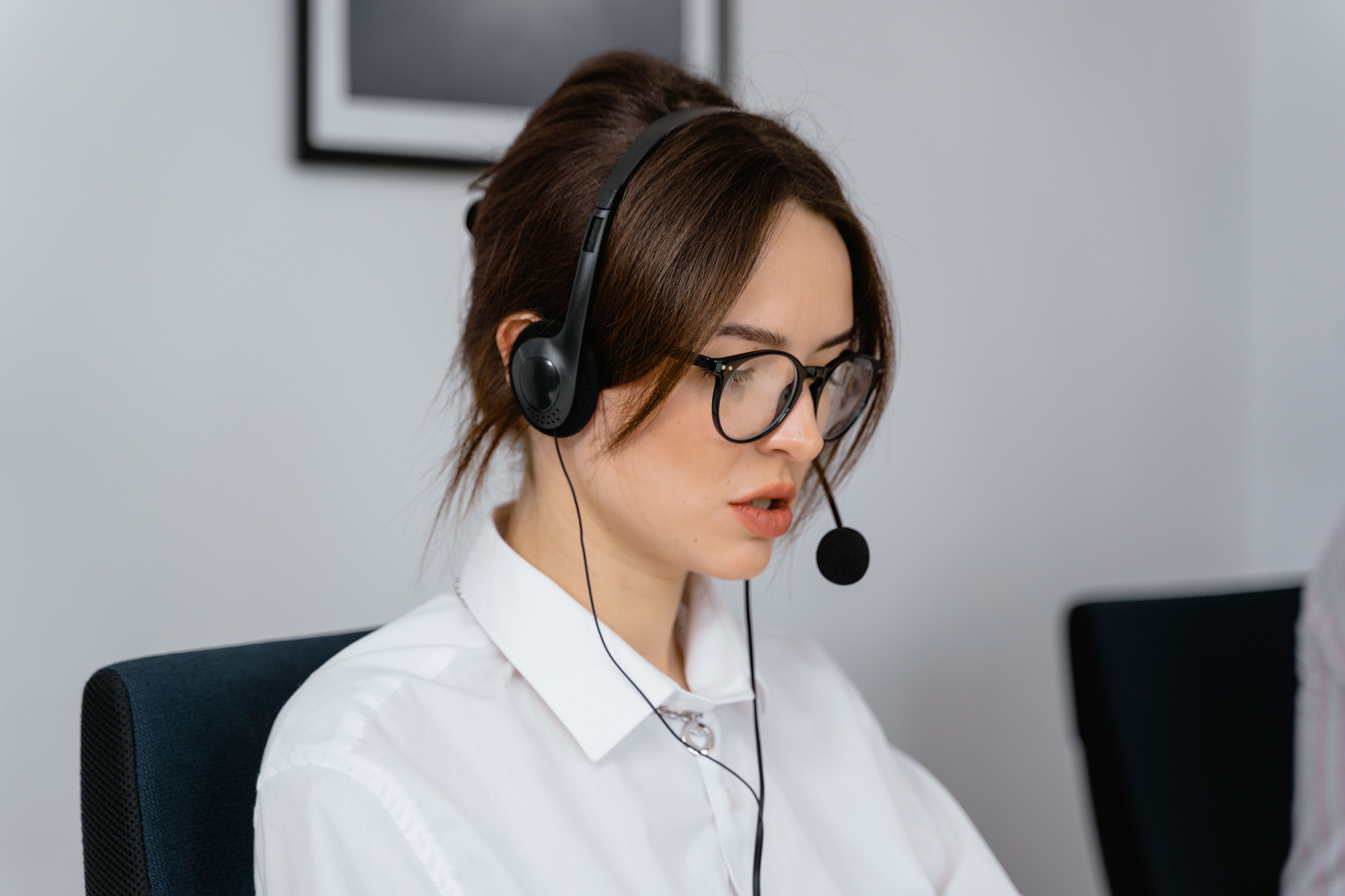 A person wearing glasses and a headset seated at a computer.