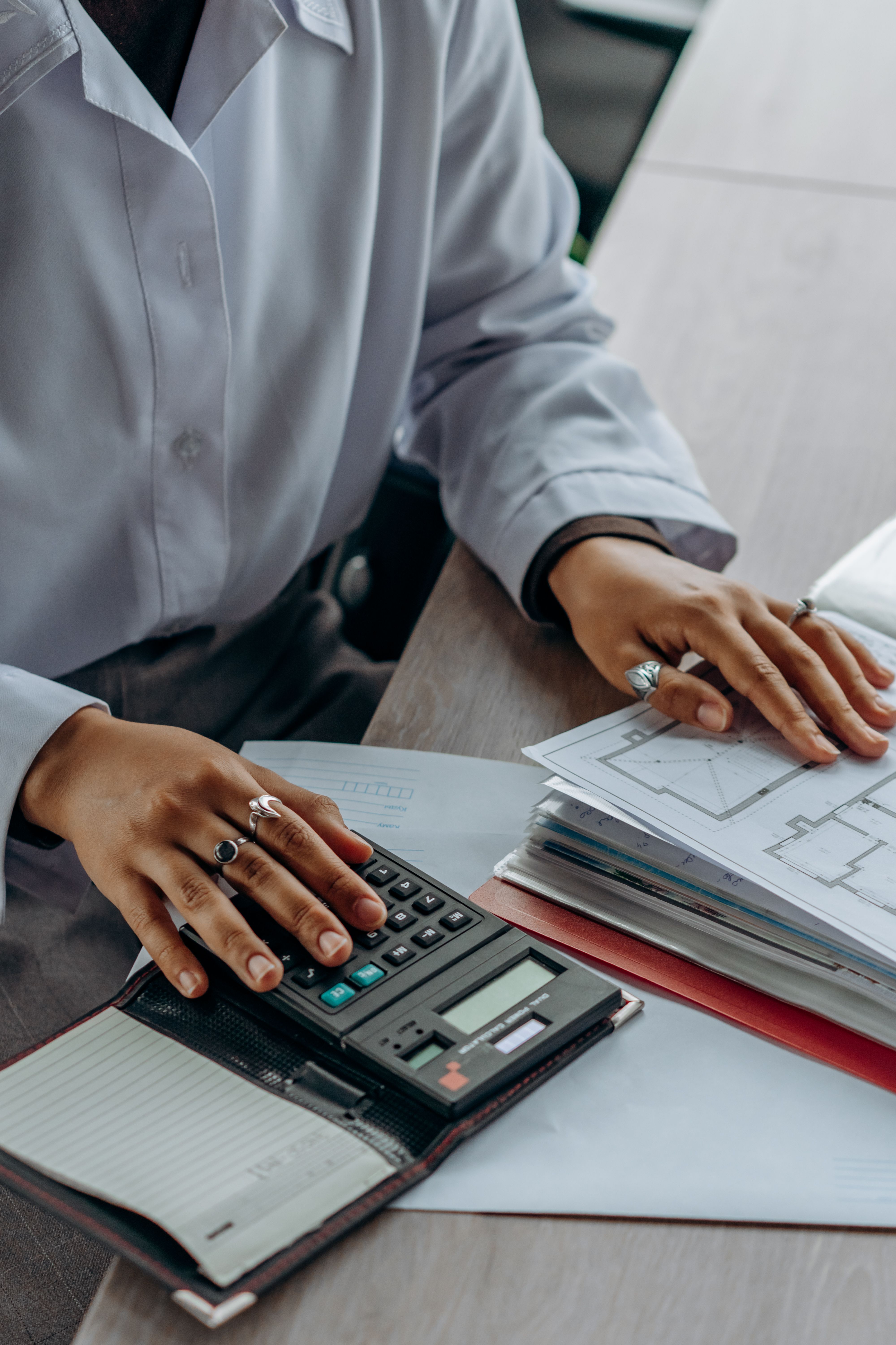 Hands using a calculator beside papers on a desk.
