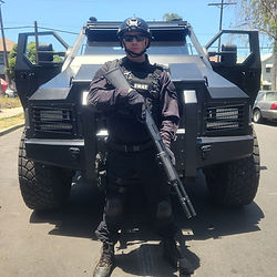 Joshua Keller Katz on set of The Rookie dressed as a SWAT officer in full tactical gear with a shotgun. Standing in front of a Bearcat armored vehicile. 