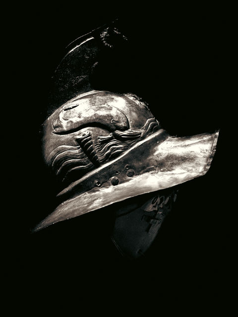 The image shows a Gladiator Helmet with light reflecting off the metal against a black backdrop.