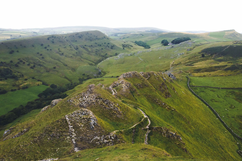 The image shows an expansive view across the ridge of a mountain peak, with multiple stone pathways visible and more hills in the background.