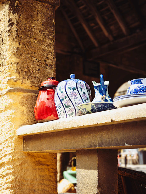 The image shows a ceramic jug, earn and several plates placed on the stone banister of a market square building.