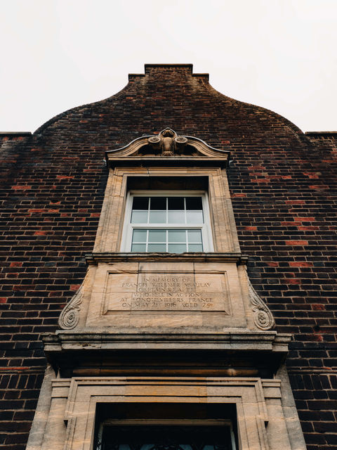The image shows a memorial plaque above a doorway and below a stone window frame.