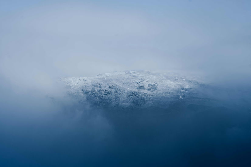 The image shows snow on the top of Loadpot Hill in the Lake District, the summit visible through a gap in the cloud lines.