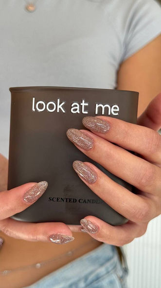 Sparkly neutral nails holding a candle saying look at me.