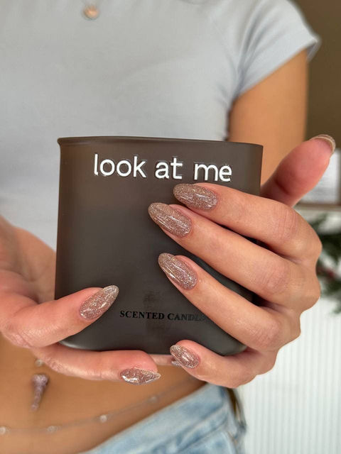 Sparkly neutral manicure on long oval nails holding a candle