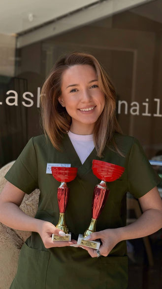 Smiling lash and nail artist holding two trophies