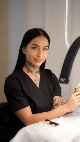 Professional lash artist with neck tattoos at her workstation