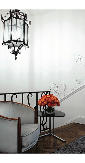 A moment of quiet glamour on the landing, where a Paul Follot armchair in pale grey velvet offers a gracious pause beside a sweeping stairwell adorned with a whimsical mural. A Tecta Bauhaus side table in black anchors a simple yet cinematic arrangement of fiery orange roses, a small reminder that even transitional spaces deserve their own narrative. Wrought iron balustrades and herringbone floors add a Parisian undertone, letting this corner speak softly of elegance without insisting upon itself. It is CAL’s signature: interiors that hold a point of view, without ever needing to shout.
