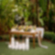 Eye-level view of a round wooden table set up outdoors with tropical plants in the background