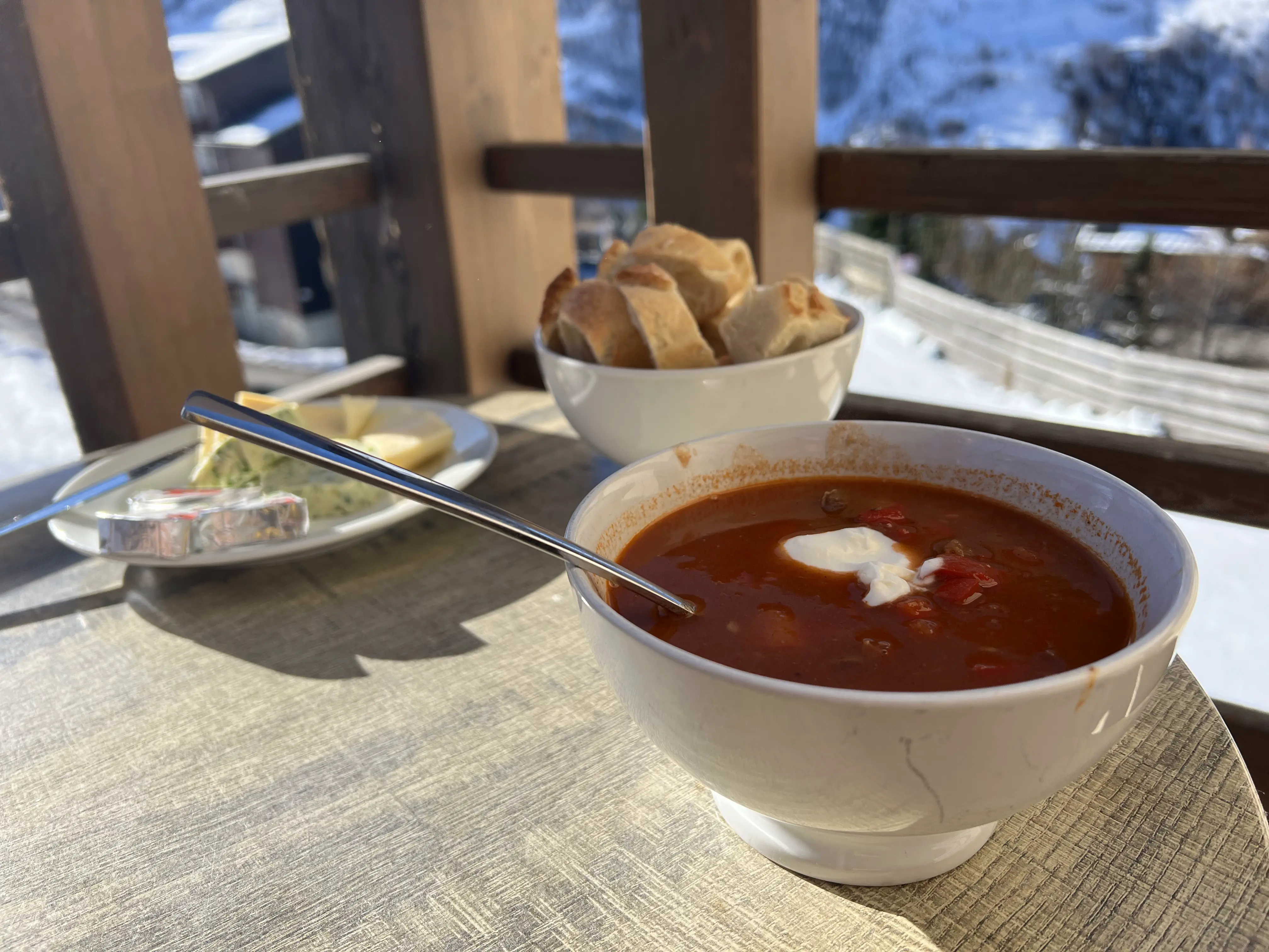 Zelfgemaakte goulashsoep met brood en kruidenboter en op de achtergrond de ski piste