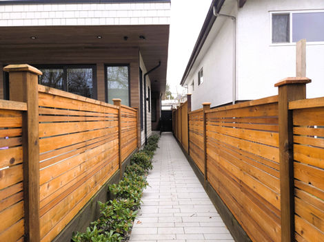 Rear unit entrance along a narrow side walkway between wood fences, leading to a covered door recess with exterior lighting.