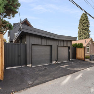 Lane view of a detached garage with dark doors and a sloped roof, set behind fencing at the rear of the duplex lot.