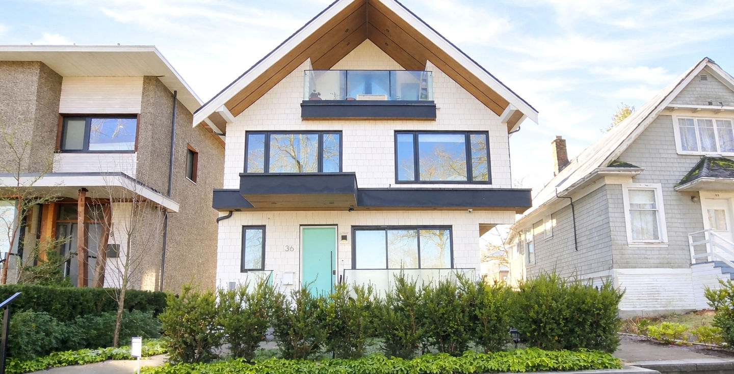Front perspective of a two and a half storey front and back duplex in Riley Park with a gable roof, warm wood accents, and a landscaped front setback.