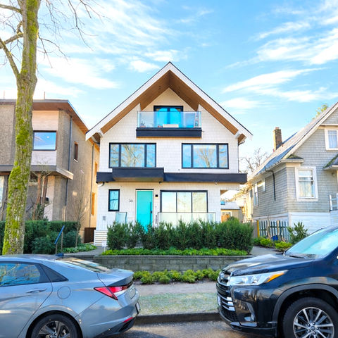 Streetscape view of the Riley Park duplex between neighbouring homes, showing the gable roof form, upper level glazing, and planted frontage along the sidewalk.