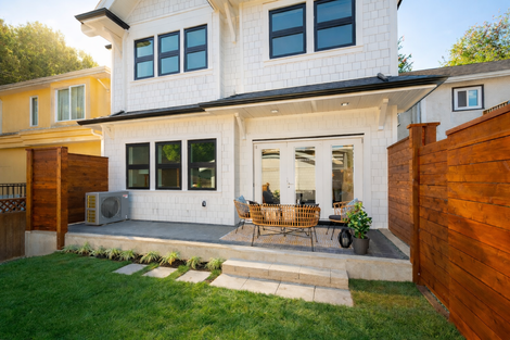 Rear patio with concrete steps, lawn, and wood fencing, opening from the duplex through wide windows and doors at the main floor.