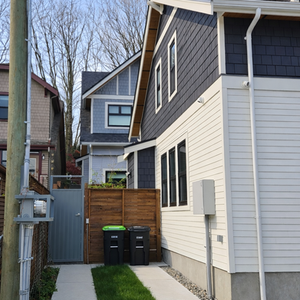 Rear yard parking pad and paved access path between buildings, with fencing and planting defining the shared courtyard approach.