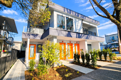 Northwest angled view of the rental building showing the corner entry condition, upper level balconies, and landscaped frontage along the sidewalk.