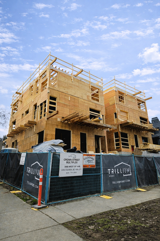 West 35th Multiplex - Under construction photo of a multiplex on a corner lot, showing wood framing for multiple buildings and the overall three storey massing.
