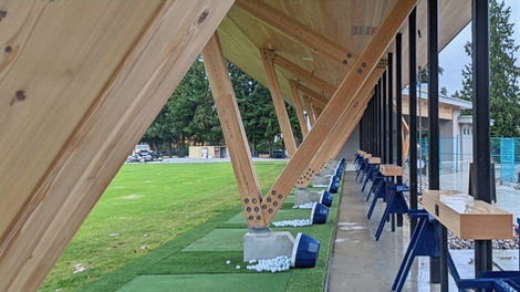 Close view of individual driving range hitting bays with mats and seating under the timber canopy facing the range.