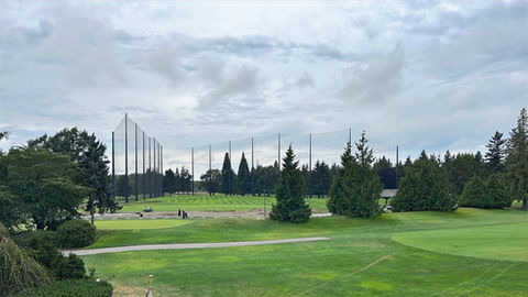 Wide view of the Marine Drive Golf Course driving range with tall perimeter netting poles in the distance and open fairway turf in the foreground.