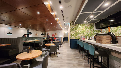 Interior dining area with banquette seating, round tables, warm ceiling finishes, and large windows providing waterfront daylight.