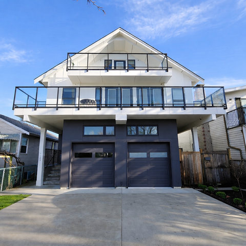 Front perspective of a two and a half storey stacked duplex with an attached double garage, upper balcony railings, and entries on both sides of the garage.