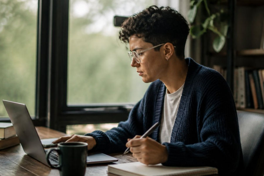 A person sitting at a desk with a laptop, browsing an inclusive therapy directory website, with a notepad and pen nearby for jotting down potential providers