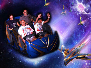 People on a roller coaster in space-themed setting, smiling and raising hands. Riders wear "Ratatouille" shirts. Colorful galaxy background.  This is Guardians of the Galaxy at Disney's Epcot.