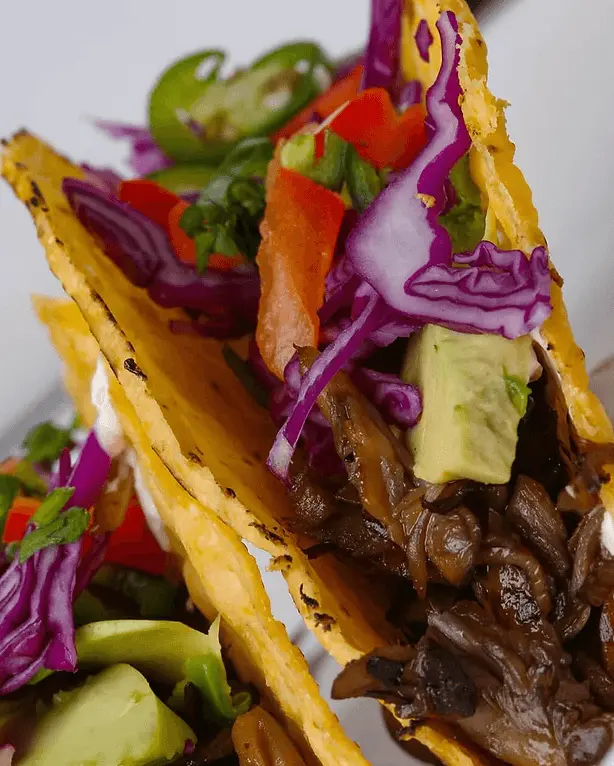 Closeup of a maitake taco with avocado, cabbage and tomato