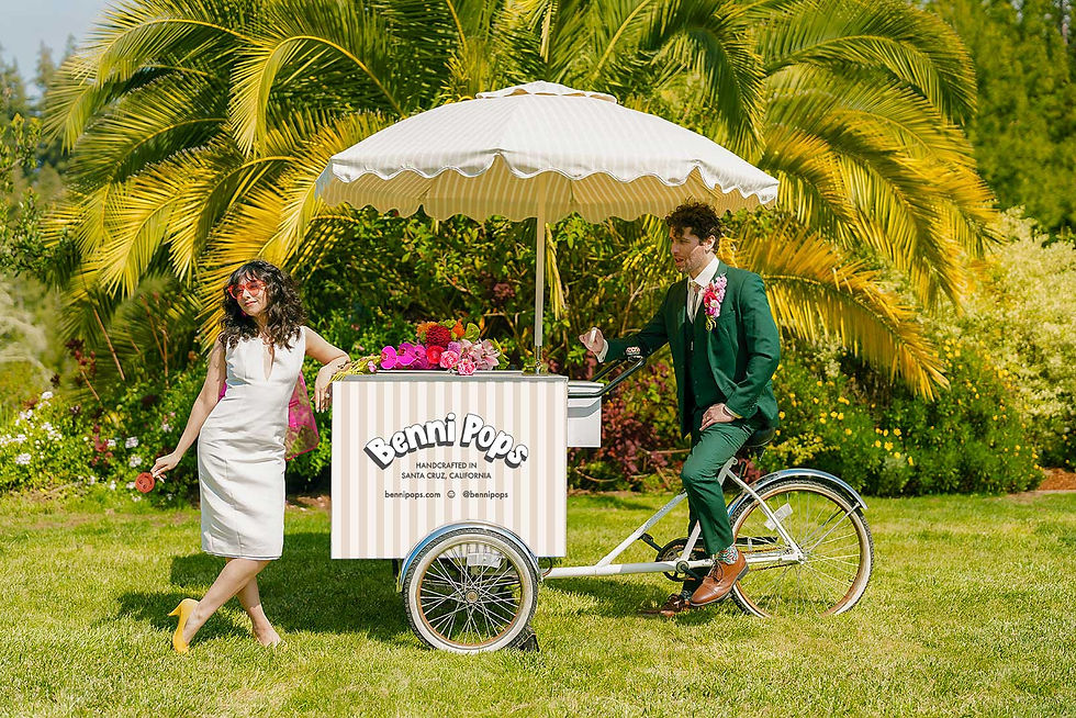 Groom and bride hold popsicles near bouquet and popsicle cart with umbrella
