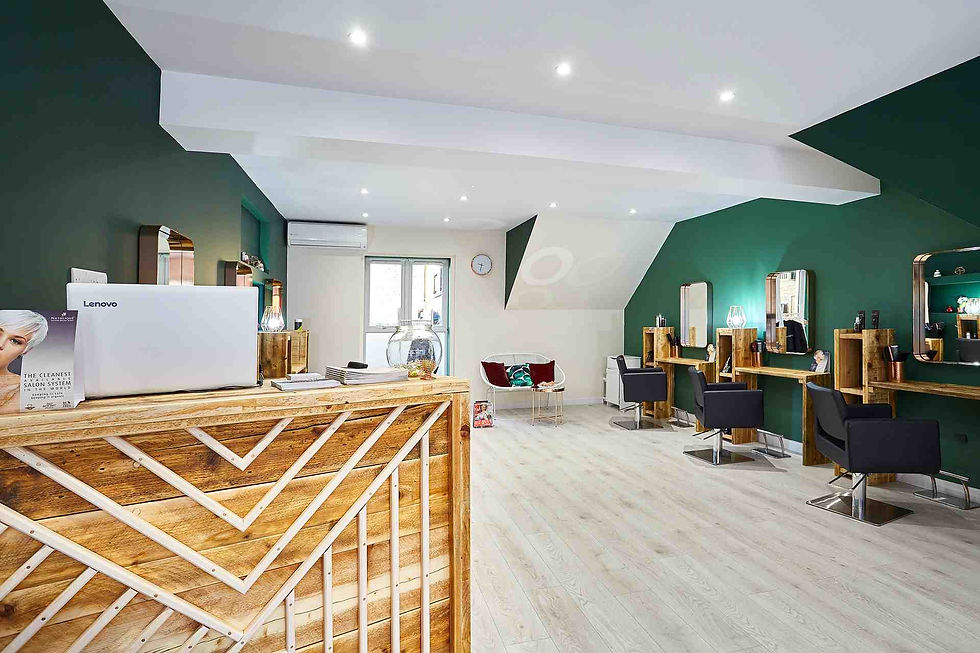 Modern salon interior with green walls, wooden accents, and black chairs. laptop on reception desk. Bright lighting and airy space.