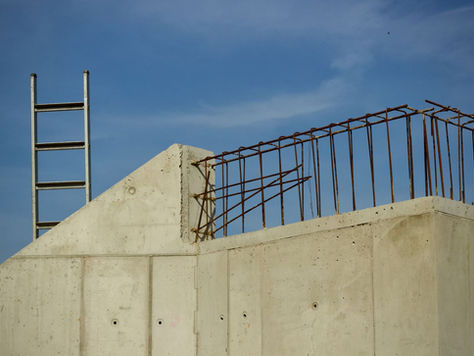 Concrete building in progress with ladder and rebar against a clear blue sky.