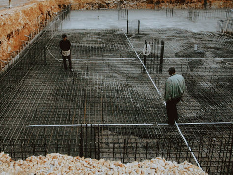 Two workers inspecting a rebar grid foundation at a construction site.